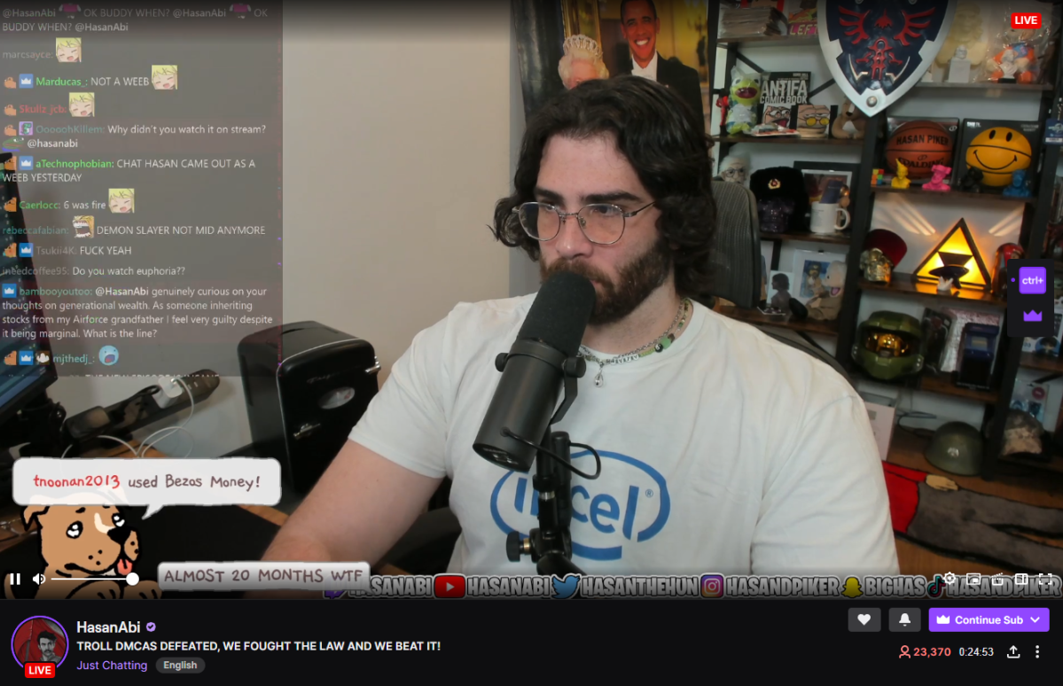 Image of Hasan Piker (brown hair, beard, muscular build) sitting at a desk streaming with his chat appearing on the screen.