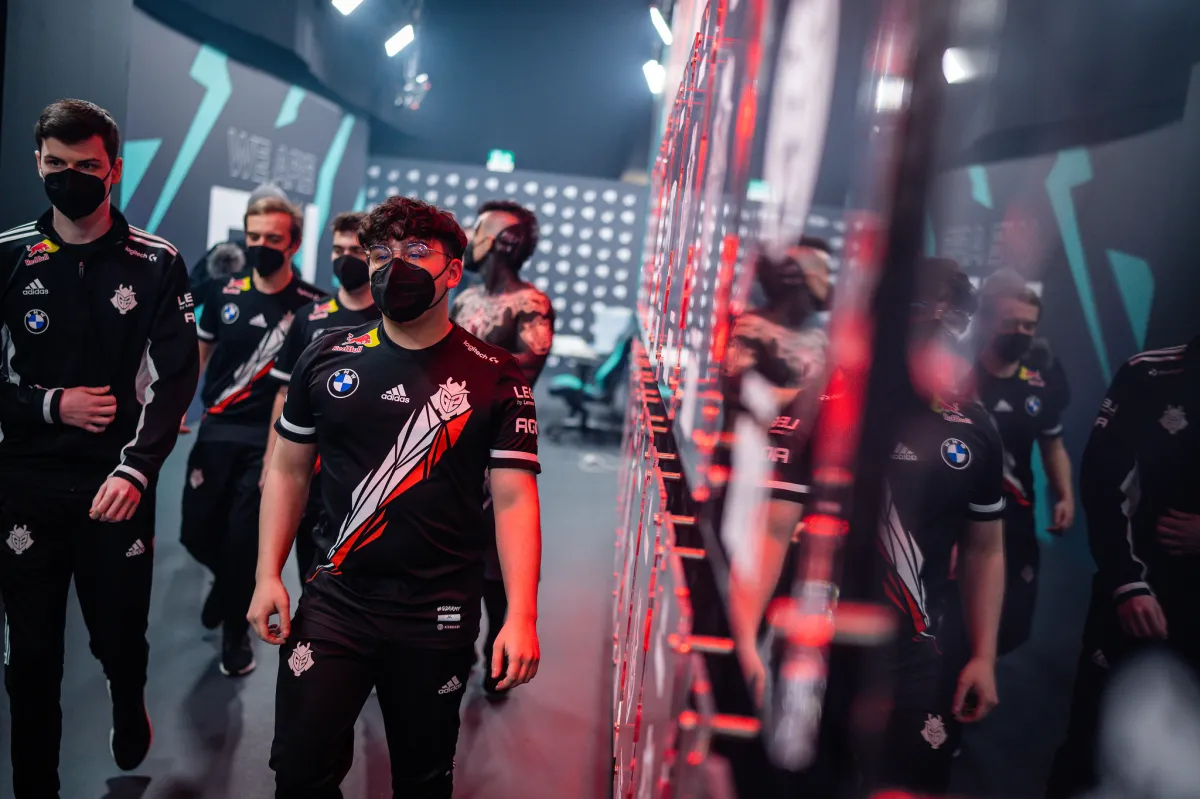 G2 players in their jerseys and wearing face masks walk down a hallway.