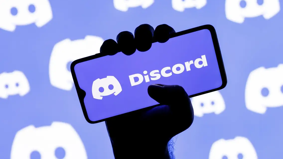 A silhouetted hand holds a phone displaying the Discord logo