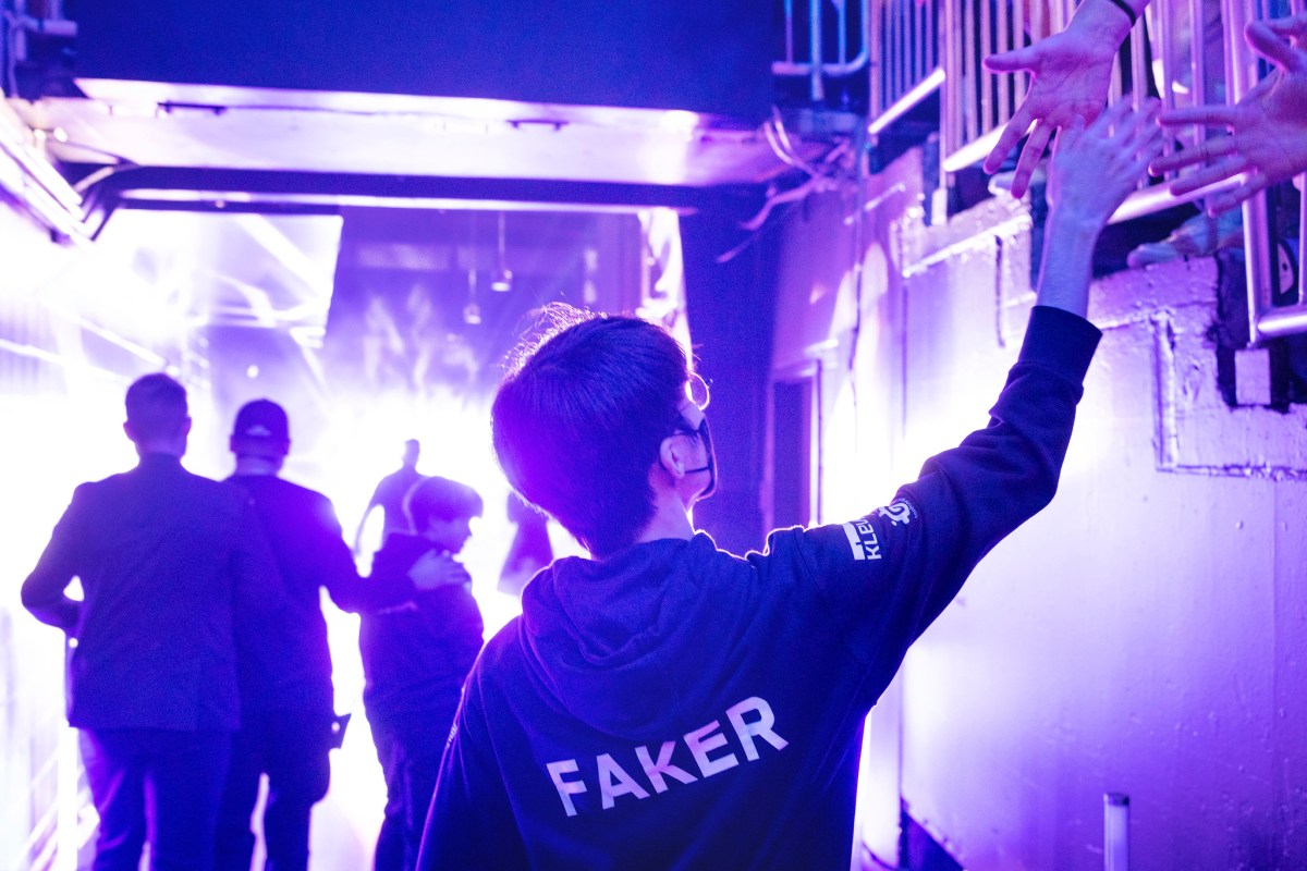 Faker makes his entrance at State Farm Arena in Atlanta, GA for the 2022 Worlds semifinals. Pictured: an over-the-back photo featuring the back of Faker's jersey as he reaches up in the crowd to shake hands with a fan.
