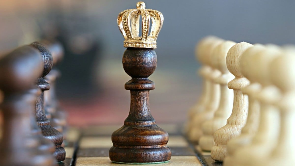 A black pawn in chess, wearing a small crown, whilst placed on a chessboard.