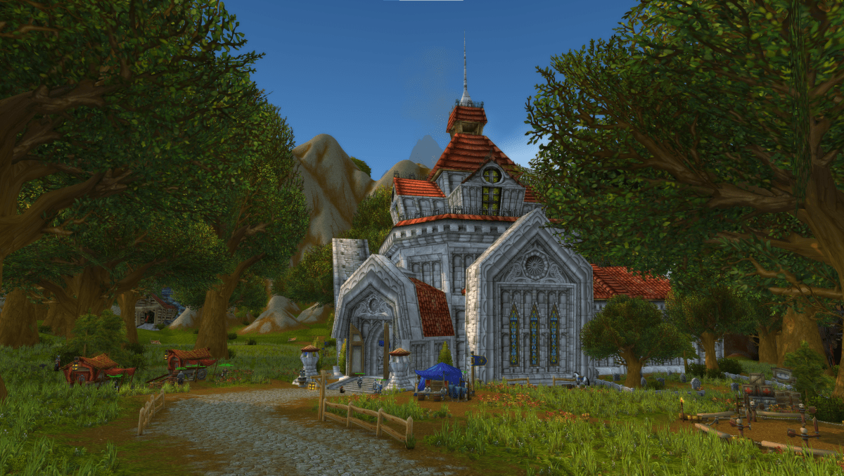 An in-game screenshot of Northshire Abbey in World of Warcraft. The road to the Abbey is pictured in the forgeround while the white and red chapel can be seen directly in the center of the image, flanked by trees on all sides.