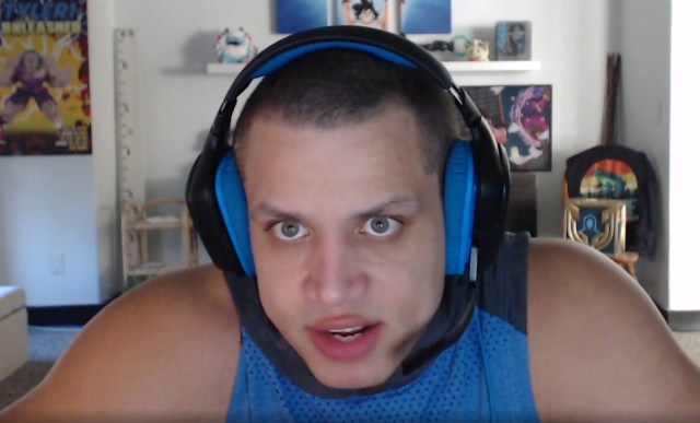 tyler1 with his headphones and a blue vest, hunched in his seat