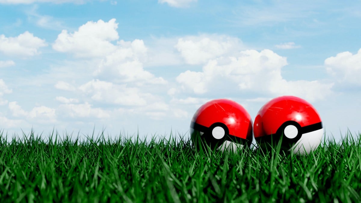 Two Pokeballs lying side by side on a field of grass.