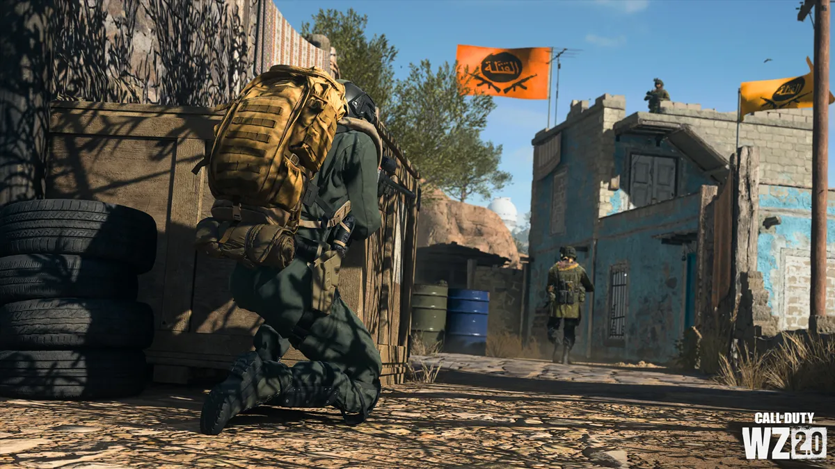 A soldier with a yellow backpack is crouched, trailing an enemy soldier outside of a stronghold with an orange flag in DMZ.