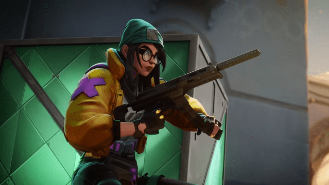 VALORANGT agent Killjoy reloading her weapon behind a green crate.