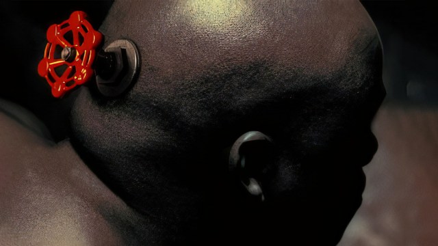 a bald man is facing away from the camera. there is a red valve attached to the back of his head