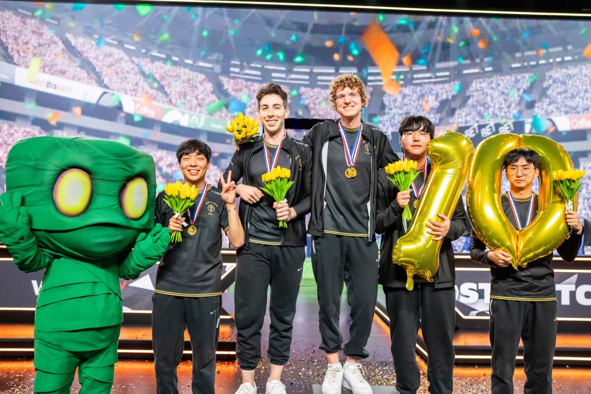 (From left to right) Huhi, Stixxay, Licorice, Gori, and River smile at a medal ceremony. Huhi is standing next to someone dressed as Amumu, and Gori and River are holding the numbers one and zero to commemorate the team's tenth win.