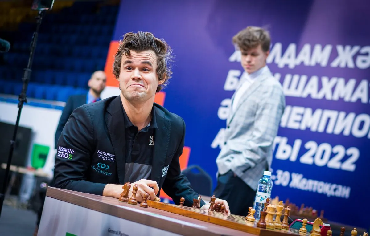 Magnus Carlsen grins while sitting at a table playing chess at the 2022 World Chess Rapid & Blitz Tournament.
