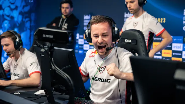 Heroic captain cadiaN cheers and fistbumps a teammate while sitting at his desk playing CS:GO.