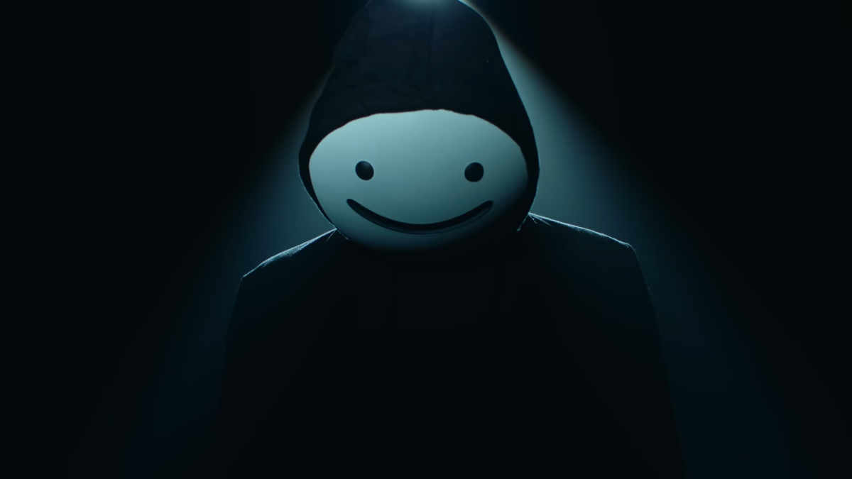 dream in his smiley face mask in front of the beam of a single light. he's wearign a dark hoodie