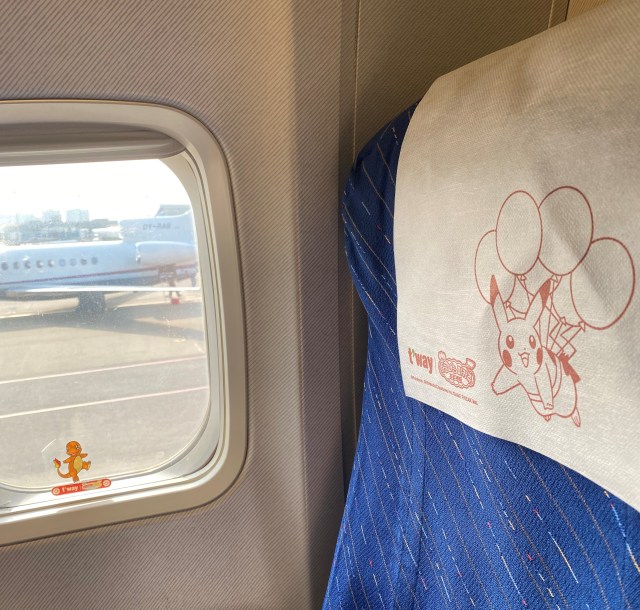 Inside a Pokémon plane, a Charmander sticker sits at the bottom of the window. The head cover on the seat features another Pikachu flying with balloons on its back.