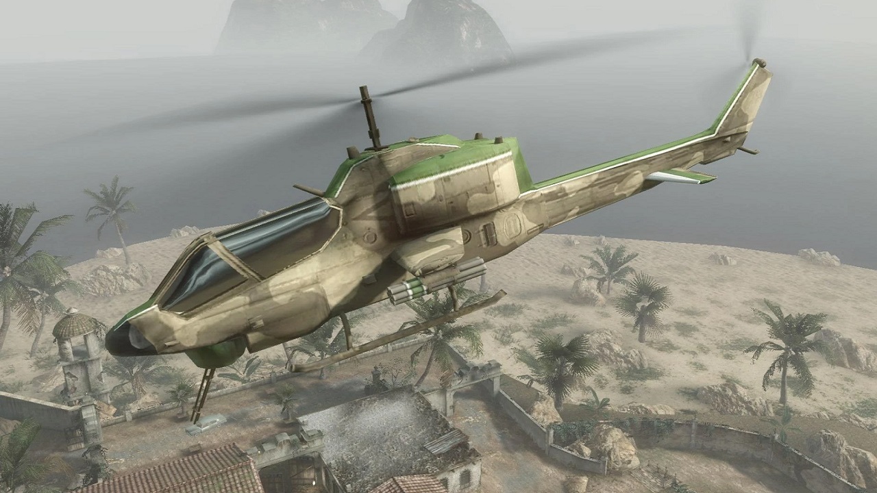 A helicopter is flying over a desert city. There are palm trees and a sandy environment in the distance.