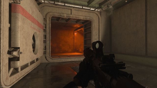 Image showcasing the Koschei Complex entrance bunker door and a gun is visible on the screen with a scope attached. Red-orange lighting lights up the tunnel entrance.