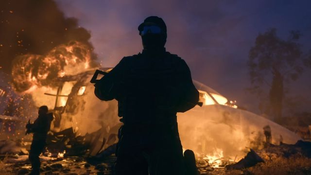 Image of a soldier standing in front of a burning plane crash wielding a weapon. Smoke plumes are being shot up into the air with a cascade of orange on show.