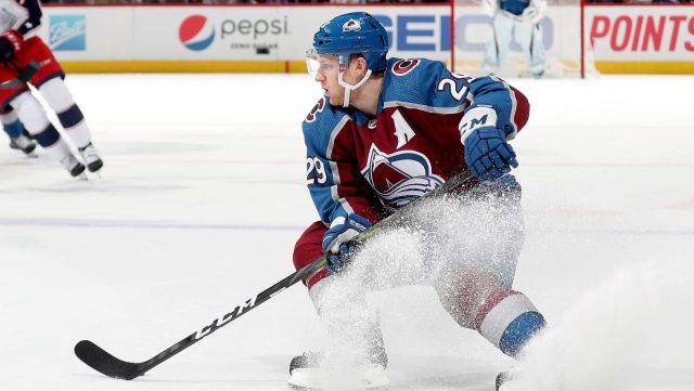 Number 29 Nathan MacKinnon wearing his away jersey and stopping as ice flies up in anticipation for a pass. 