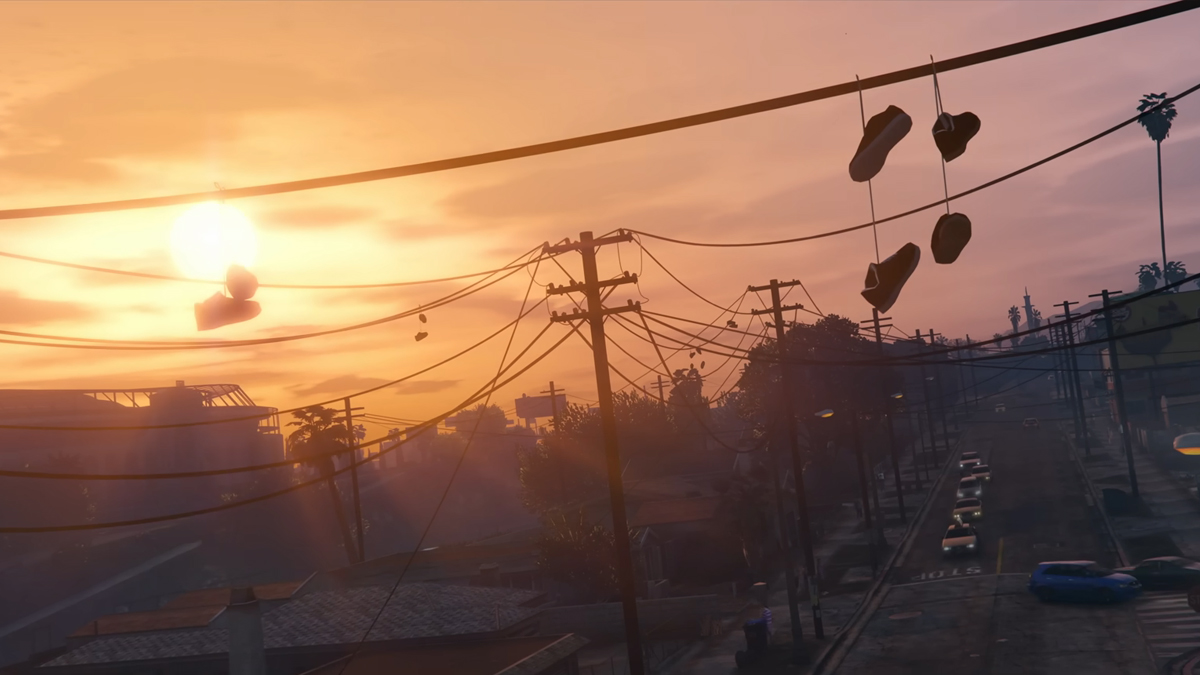 The sun sets on a suburban town with palm trees in the background and a pair of shoes draped over powerlines in GTA 5.