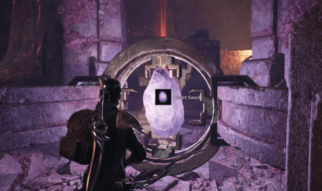 The player character in Remnant 2 stands in front of a purplish-pink crystal that's locked in a contraption. An indicator says its the Heart Seed.