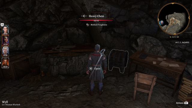 A room in a cavern with a heavy chest next to a desk, which Wyll stands in front of.