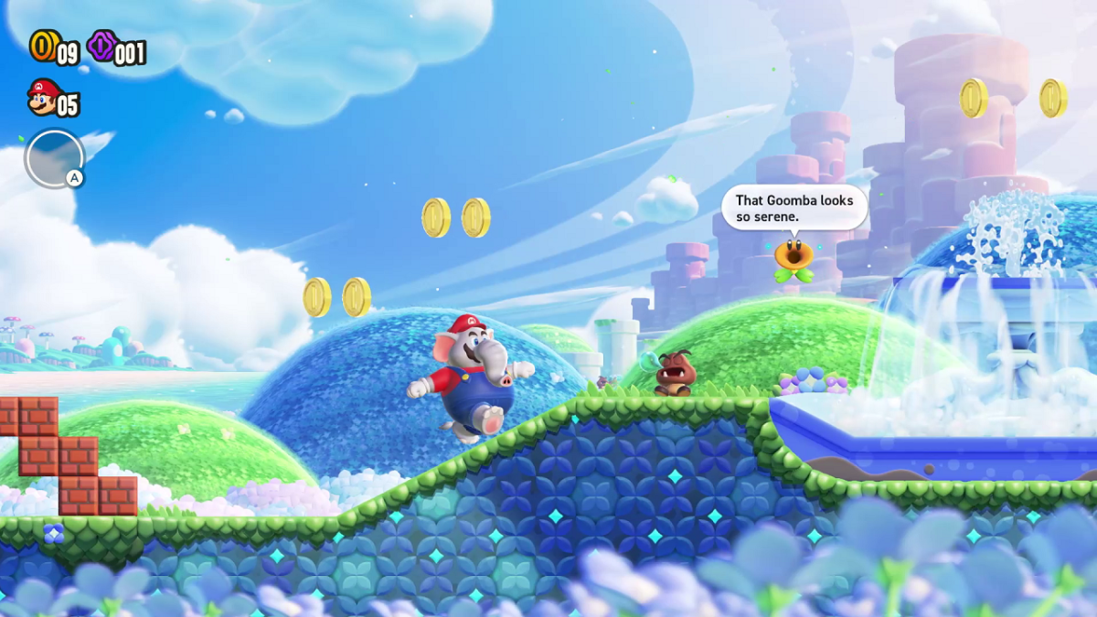 An elephant version of Mario is running, while a Goomba is standing up ahead. A small flower is talking on a hill in the background.