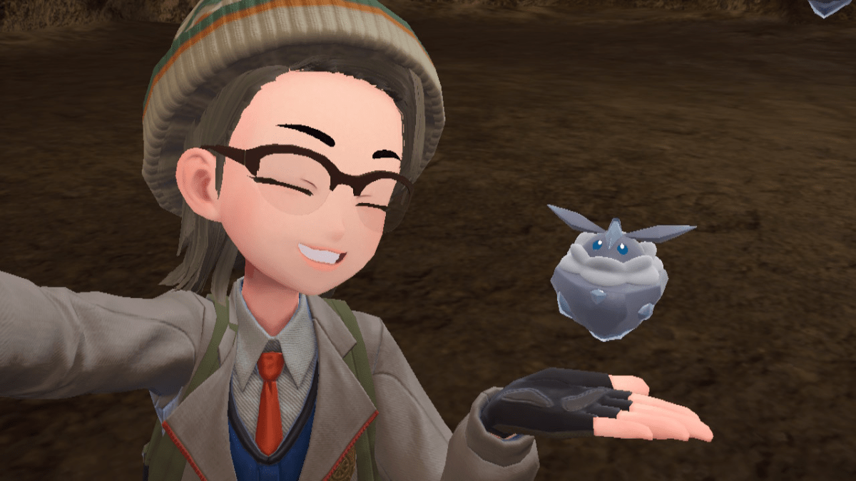 A Pokémon trainer in The Teal Mask DLC smiles and takes a selfie with Carbink, a small blue rock-like Pokémon.
