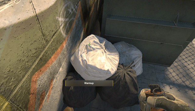 A CS2 character aimining a smoke at a bag of trash in Overpass.
