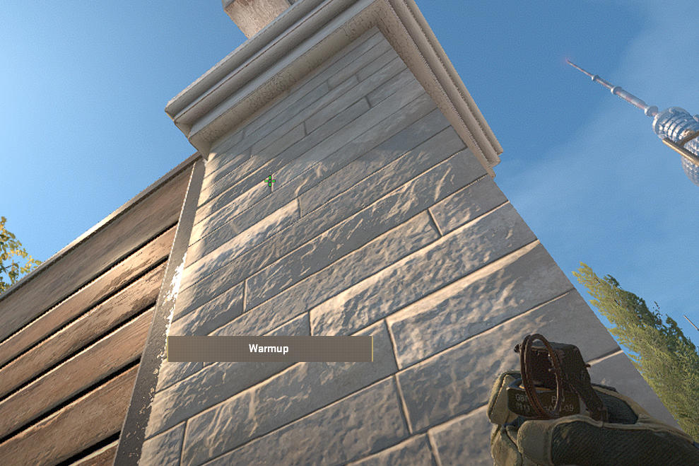 A CS2 character holding a smoke up towards a wall in Overpass.