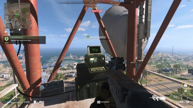 A player holds a gun while standing on a radio tower in Al Mazrah, staring at an intel contract computer in DMZ.