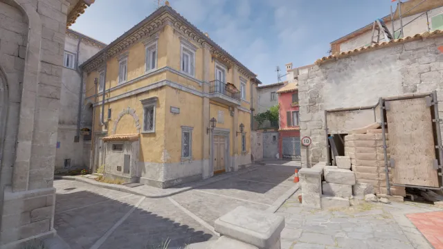 A cobblestone street and a yellow building, marking the location of the B bombsite on Inferno in CS2.