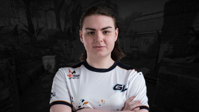 CS:GO player KittyTM with her arms crossed standing in front of an image of Ancient, a CS:GO map.
