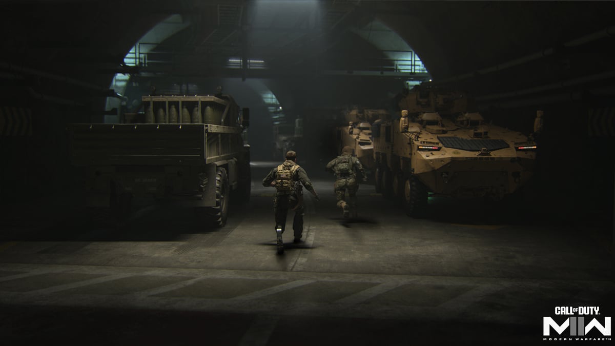 Two Shadow Company soldiers stand in a garage next to two armored vehicles in DMZ.