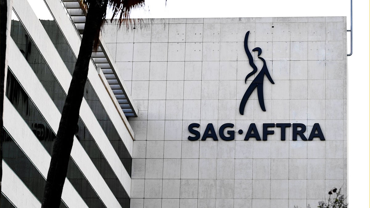 The SAG-AFTRA logo on a building at the Los Angeles headquarters for the union, with a palm tree in front of it.