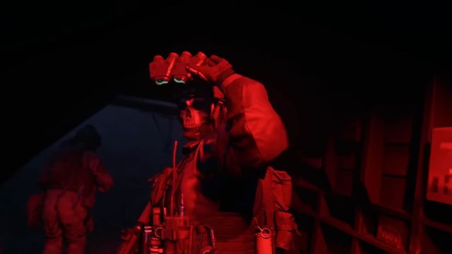 Image of the character Ghost in a helicopter with red lights shining on him. There are night vision goggles being held and Ghost's signature skull mask is in view too.