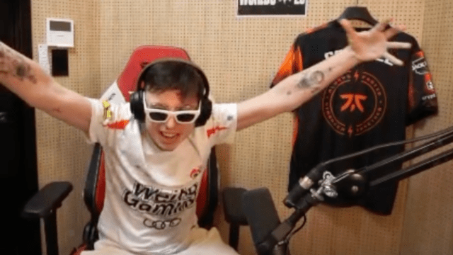 Streamer Caedrel extending his arms up in the air after ripping off his G2 jersey to reveal a Weibo one. He's wearing sunglasses indoors.