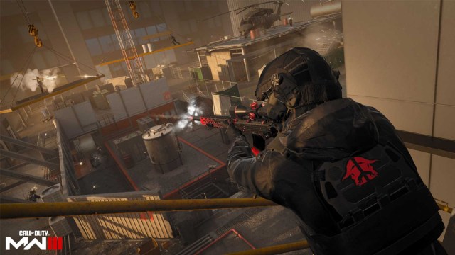 A soldier with a backpack stands on a building looking down at a rooftop as a firefight takes place in Call of Duty: Modern Warfare 3.