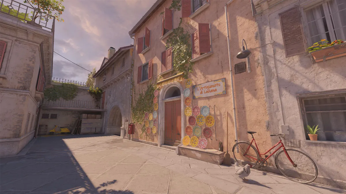 A paved sidewalk outside a yellow building covered in art with a red bike next to it on Italy, a map in CS2.