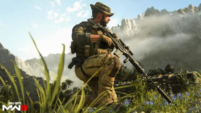 Captain Price kneeling in a grass field, holding a sniper rifle with a silencer attached. 