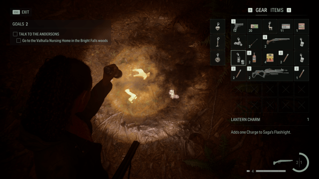 Saga's flashlight illuminating the Lantern Charm on the ground in the forest in Alan Wake 2.
