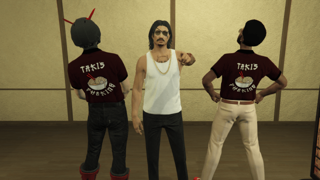 Three characters in GTA 5, two on the outsides both have their backs turned, wearing shirts labelled "Pho King". The man in the middle wears a white tank top and a gold chain, with both an eyepatch and sunglasses. He's pointing at the camera.
