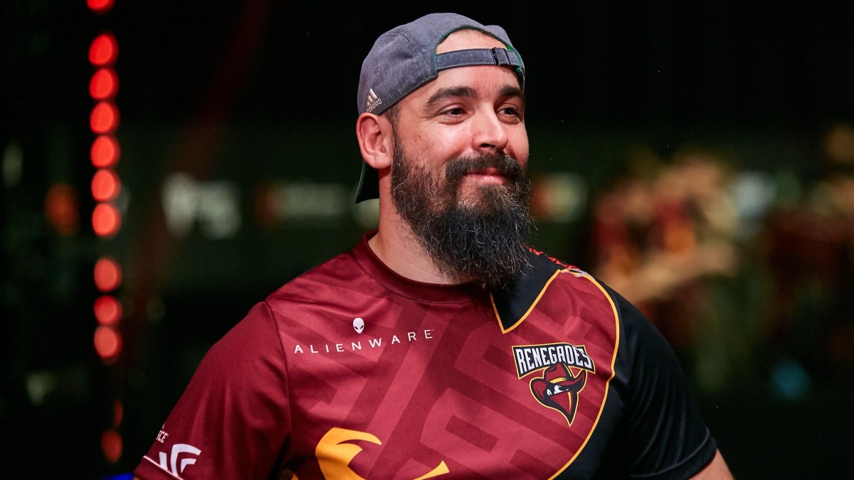 Photo taken of male Counter-Strike coach Kassad while he was attending StarLadder 2019 with Renegades. He's wearing Renegades' red jersey and a blue Adidas cap. He also had a long beard back then.