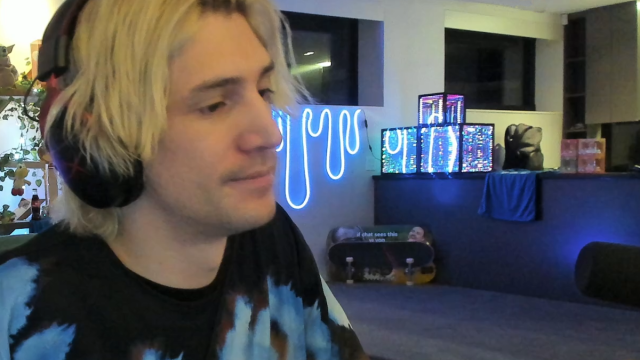 xqc off to the side of the screen weating black headphones and bleach blonde hair