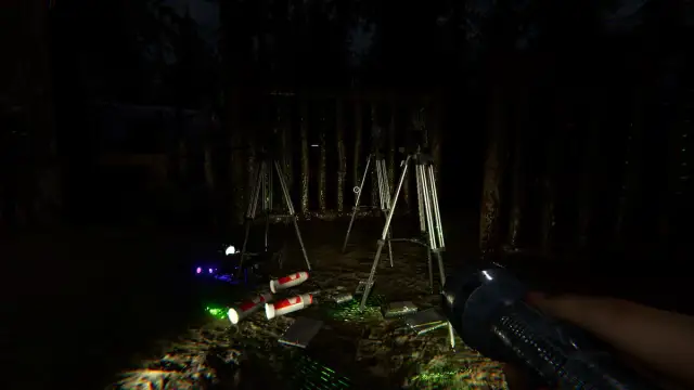 A bunch of ghost hunting equipment on the ground by a wooden gate in Phasmophobia.