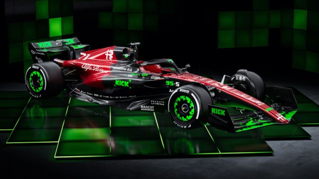 A sleek car with front and rear wings is adorned in a dark red and black livery. Neon green elements are dotted over the main car and wheels. It sits on a chequered black and green surface.