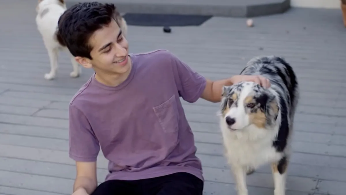 young guy in a purple shirt petting his fluffy white dog