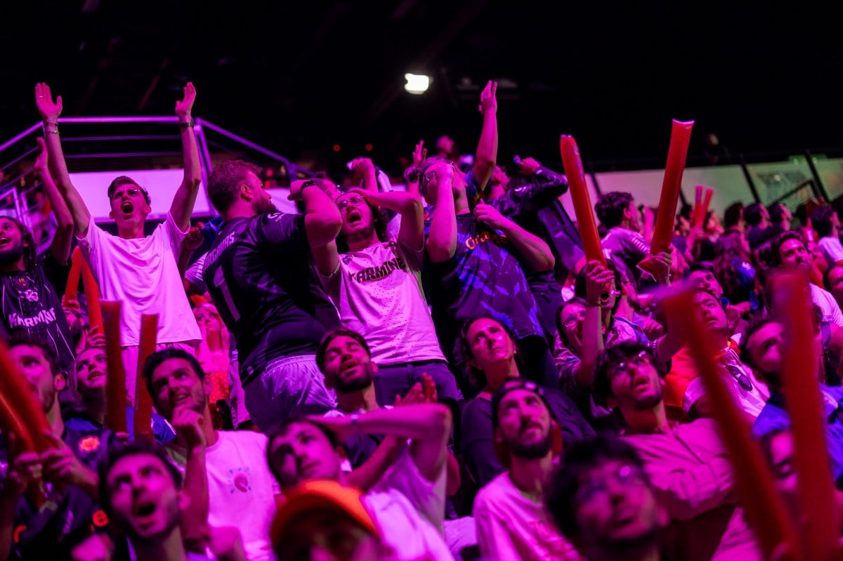 LoL fans cheering in the crowd, highlighted by a pinkish/purple light.