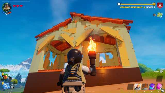 A LEGO Fortnite player stading infront of a double shack while holding a torch.