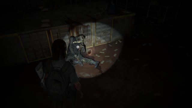 Ellie shines a torch on a dead body with a pump shotgun