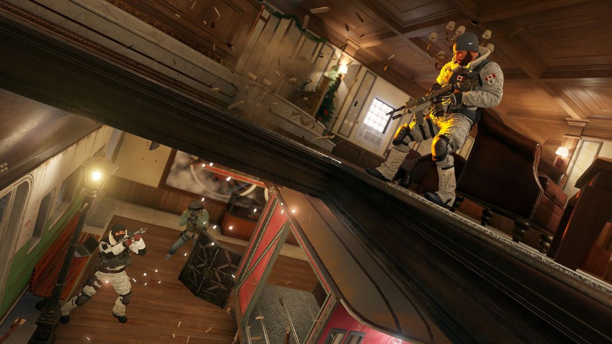 Image of Rainbow Six Siege characters battling inside of a building. The Character Frost is aiming up at an opened hatch in the ceiling to further defend a site.