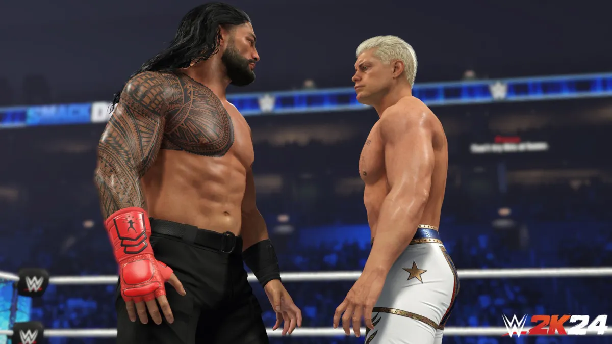 Roman Reigns, wearing black trousers and a red glove, staring down Cody Rhodes, wearing white tights.