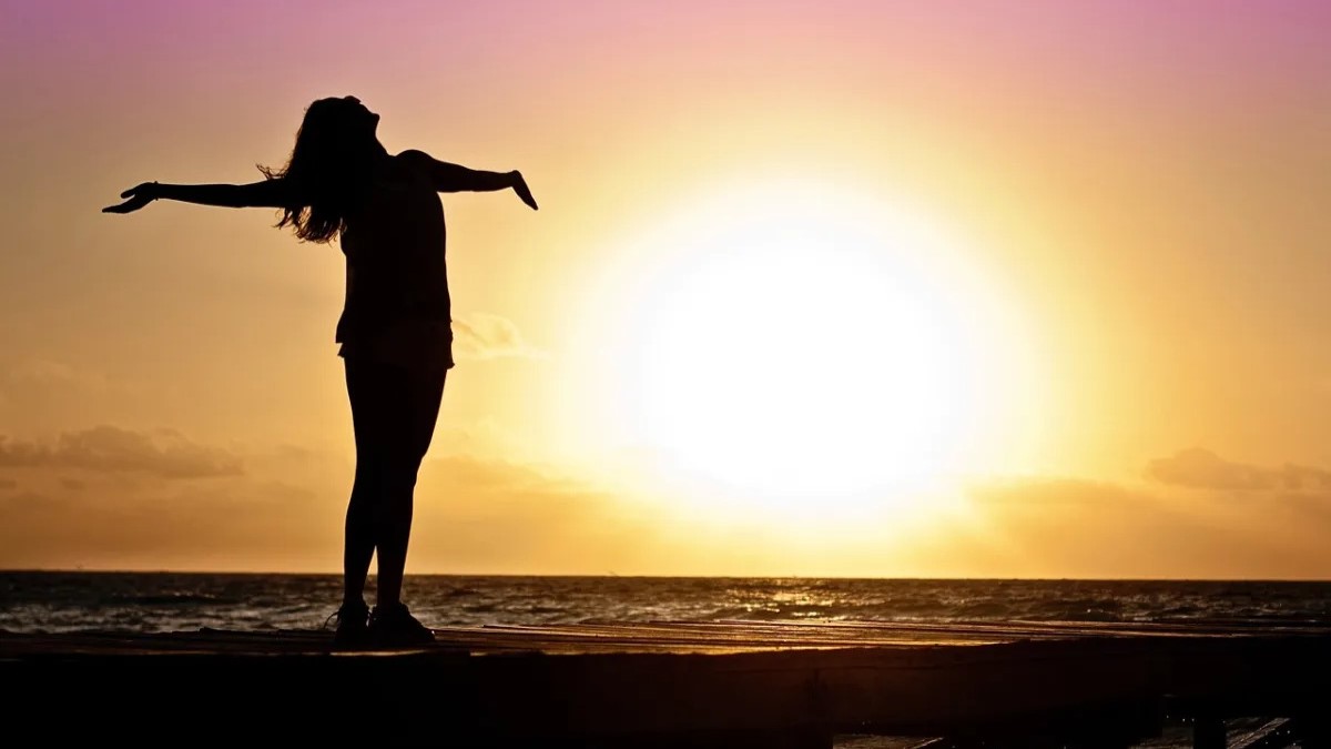 Woman is looking at the Sun with her arms stretched